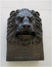 An iron lion-head mailbox on the front wall of the post office