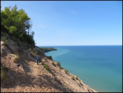People admiring Superior Lake and the dunes. In the distance can be seen Au Sable Light Station - a little dot on the small peninsula. This is a very good spot to see the depths of the water along the shore. You can notice lighter shades of the water that indicates the shallows. Reason for the shipwrecks in the that area.